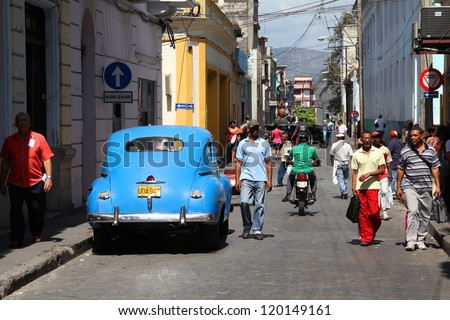 SANTIAGO, CUBA - FEBRUARY 10: People walk past old car on February 10, 2011 in Santiago, Cuba. Recent law change allows the Cubans to trade cars again. Cars in Cuba are old because of the old law.