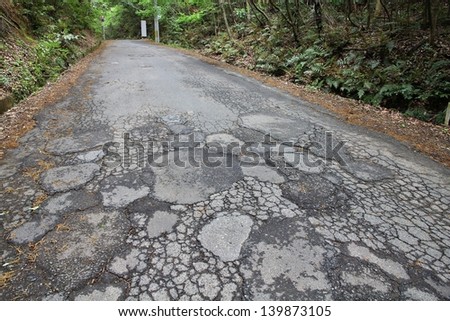 Damaged road in Japan - cracked asphalt blacktop with potholes and patches