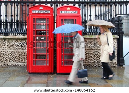 London, United Kingdom - Red Telephone Boxes In Wet Rainy Weather. Wet Pedestrians With Umbrellas.
