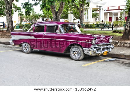 HOLGUIN, CUBA - FEBRUARY 16: Cubans sit next to an old car on February 16, 2011 in Holguin, Cuba. Recent change in law allows the Cubans to trade cars after it was forbidden for many years.