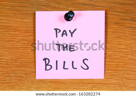 Sticky note with home expenses message: pay the bills. Bulletin board.
