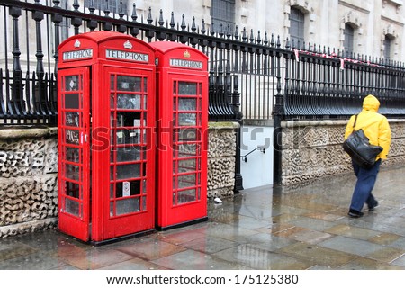 London, United Kingdom - red telephone boxes in wet rainy weather. Wet pedestrian in a yellow rain coat.
