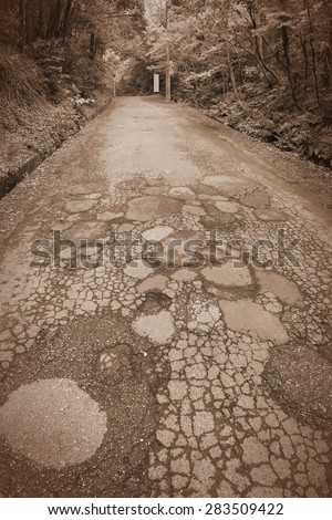 Damaged road in Japan - cracked asphalt blacktop with potholes and patches. Retro style sepia image.