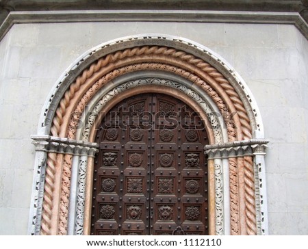 Wooden door with huge nails and interesting bas-relief carvings on a facade of a baroque basilica in Bergamo, Lombardy, Italy.