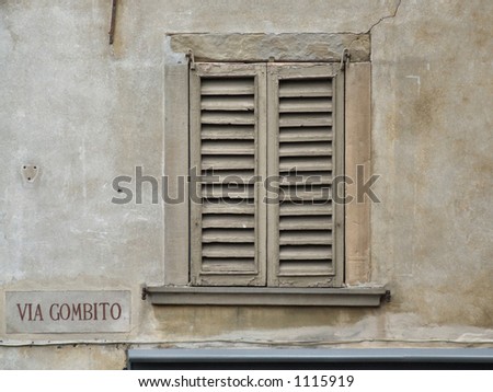 Interesting old window with closed shutters - sad scenery, historic architecture, dark place, touristic town. Name of a street. Nice, rough, coarse surface of the old wall.