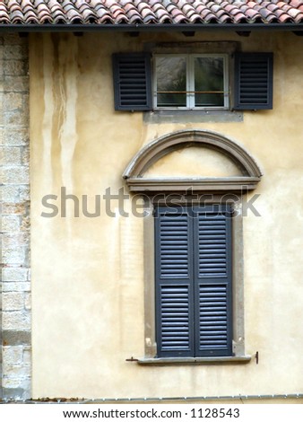 Two old, beautiful windows and a yellow wall with slate roof. A residential building elevation in Bergamo, Italy, Lombardy.
