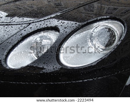 New car front lamps and black bonnet. Water drops on metal surface.