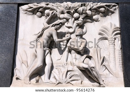 Milan, Italy. Old biblical scene sculpture at the Monumental Cemetery (Cimitero Monumentale). Religious art depicting Adam and Eve picking the fruit in the garden of Eden.