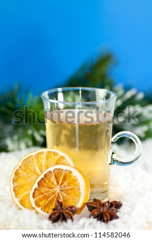 Tea with hot lemon. The glass is standing outdoors in snow. Two slices of orange and star anise are lying in the snow too. In the background you can see fir branch and the dark blue sky.