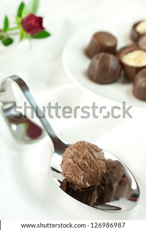 Sweet dreams - a delicious chocolates on a dessert spoon. In the background are a few different chocolates on a little plate.