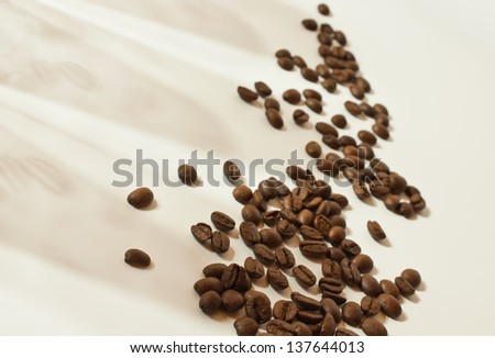many coffee beans on cream-colored background with shadows of the beans