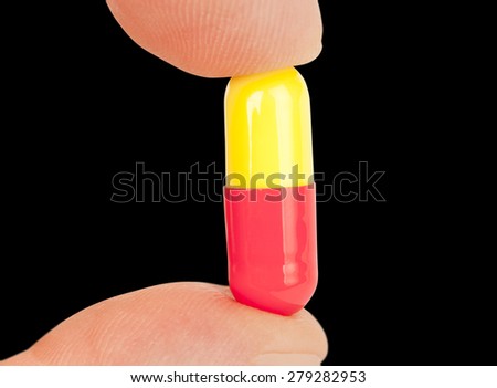 Fingers hold the capsule pills isolated on black