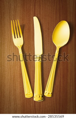 gold fork, knife and spoon over wooden table