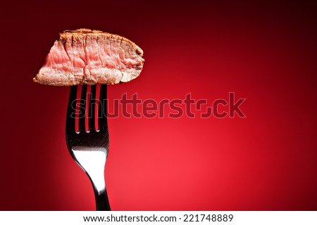Piece of a grilled steak on a fork isolated on red