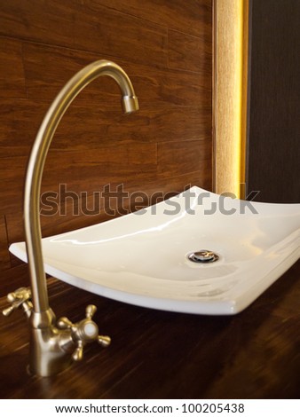White sink with golden basin mixer and wooden background