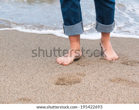 Detail of male feet at the beach with a wave of foaming water