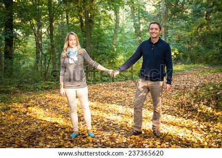Happy young pregnant couple in love holding hands on the walk in autumn nature