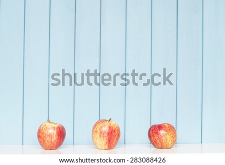 tree red apples on the shelf on blue wooden background