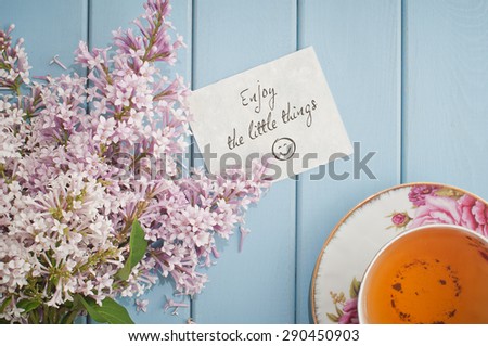 Motivational card quote enjoy the little things in summer bouquet of gentle blooming lilac  and tea in china teacup with saucer