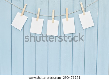 Blank photos hanging on rope with clothespins on blue wooden background