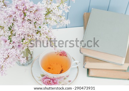 vintage books, gentle bunch of lilac and china teacup on the table on blue wooden background