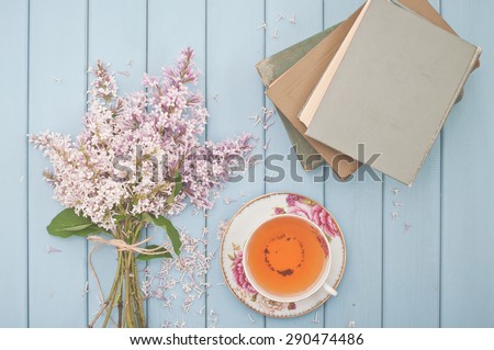 ancient books, black tea in china teacup and summer blooming bouquet of lilac