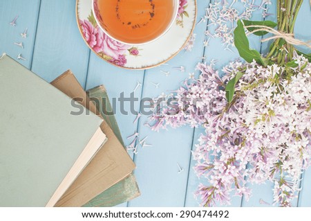 Black tea in china teacup, ancient books and summer blooming bouquet of lilac