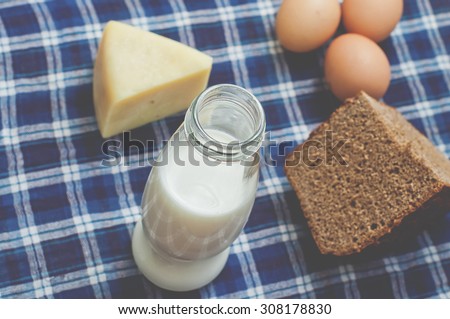 Bottle of milk, cheese and rye brown bread on rustic gingham table cloth