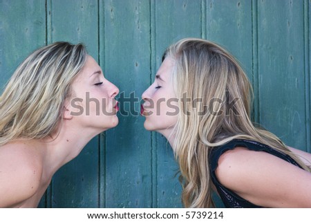 Two blond girls, face to face, on a green woody background.