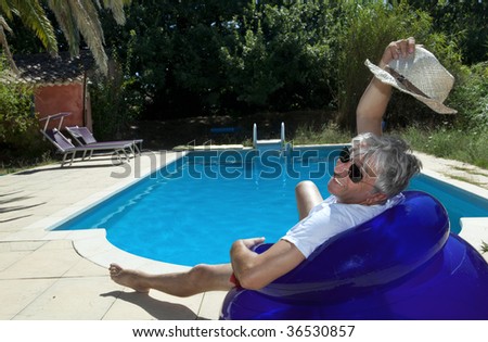 Smiling senior sitting by a swimming pool on a blue inflatable chair.