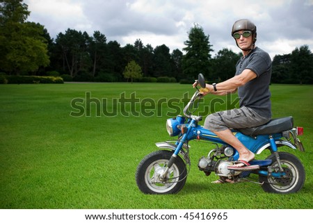 Strange biker sitting on a blue moped in countryside.