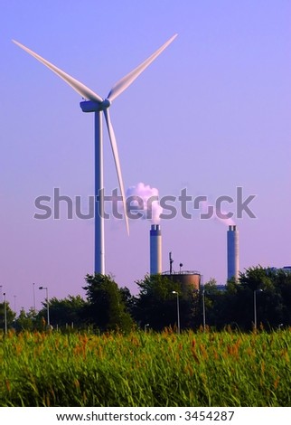 alternative energy wind turbine by the two smoking pipes of the factory