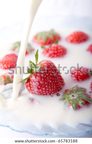 A bowl of milk with  red strawberries. Milk poured into the bowl