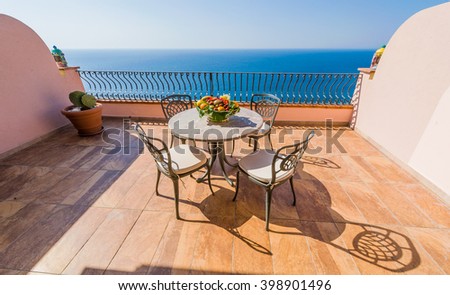 Luxury terrace balcony of exclusive seaside resort with fancy table and chairs fuit and flower bawl and full sea panorama in the beautiful morning lights, Sicily, Italy