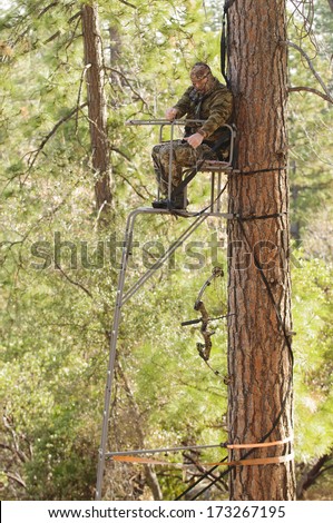 Bow hunter demonstrating good safety technique using a haul line to bring up his bow into a ladder style tree stand