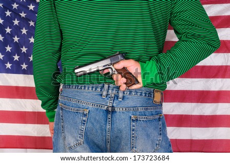 Man holding a 1911, 45 ACP behind his back in front of an American flag