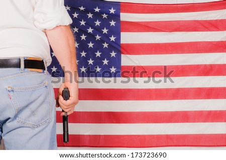 man standing in front of the stars and stripes holding a handgun