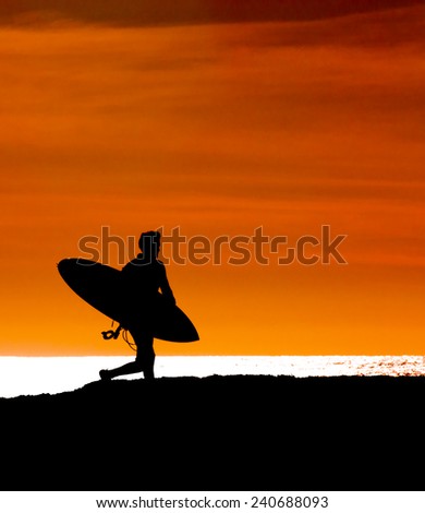 silhouetted Surfer running out to sea to get the last wave in before sunset
