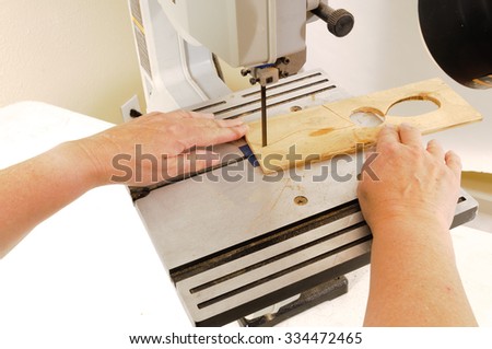 Closeup of a woman\'s hands working with a band-saw to cut an intricate shape in a piece of plywood