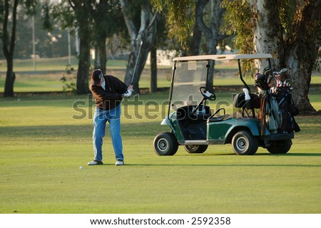 Golfer in mid swing with head of club in motion & cart