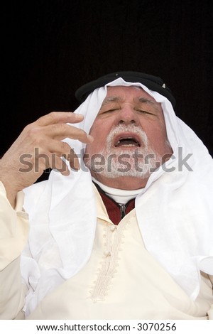 Arabic looking gentleman in a dish-dash, traditional headdress and wearing sunglasses, making gestures during conversation