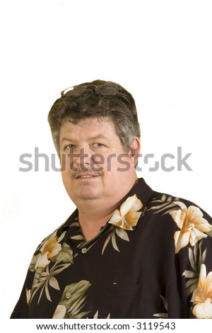 MIddle aged man wearing a black base with flowers printed on it hawaiian shirt smiling and sunglasses on his head