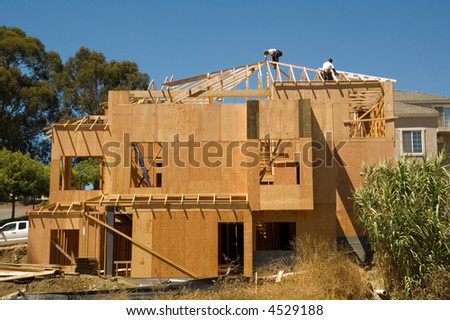 A large modern wood framed house under construction with carpenters completing the roof rafter framing