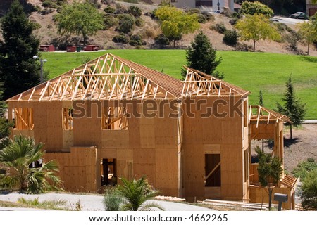 A large modern wood framed house under construction with carpenters completing the roof rafter framing