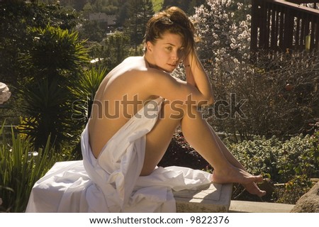 Attractive model lounging in birthday suit, wrapped in a sheet
