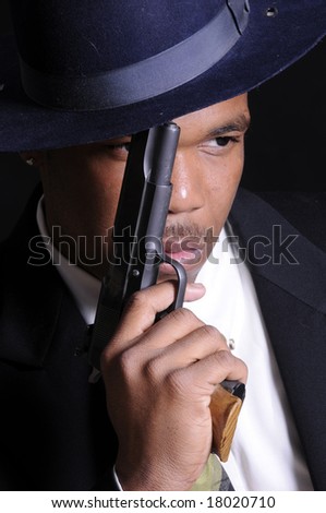 young African American man in a hat and suit with a semi automatic pistol