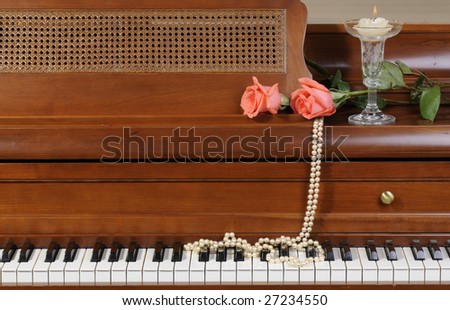 pair of peach/pink colored Roses sitting on keys of piano with candle and pearls