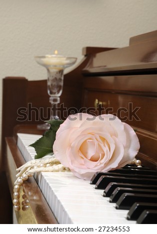 Rose sitting on piano keys with a lace glove and a string of pearls, and a candle in the background