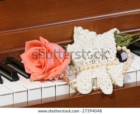 peach/pink colored Rose sitting on keys of piano with lace glove and pearls