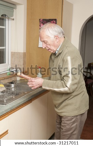 Elderly man with hearing aid working in kitchen